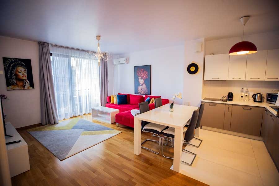 Livingul confortabil al apartamentului Riviera Suite&Lake din Cluj Napoca, cu o canapea rosie și o bucătărie complet utilată